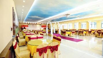 A banquet hall with round tables and chairs, a stage, and a ceiling mural.