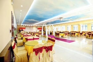 Un salón de banquetes con mesas redondas y sillas, un escenario y un mural en el techo.