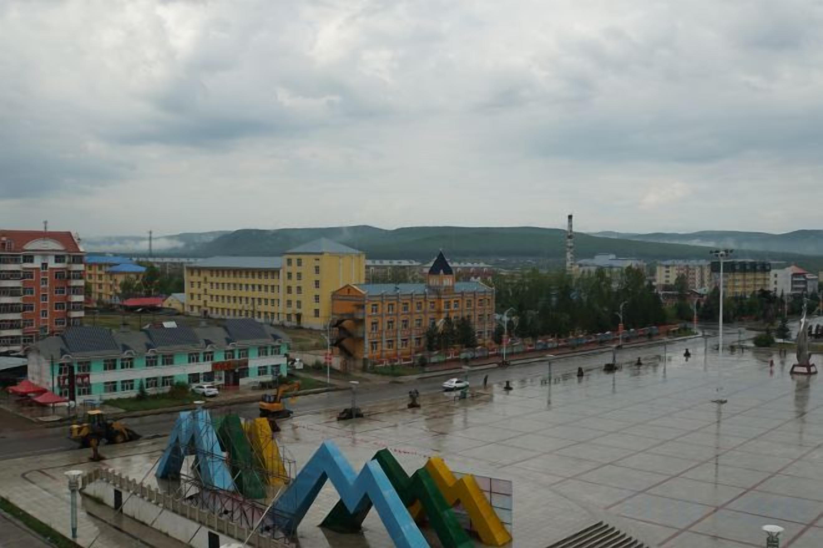 A cityscape with buildings, a large open square, and a distant mountain range.