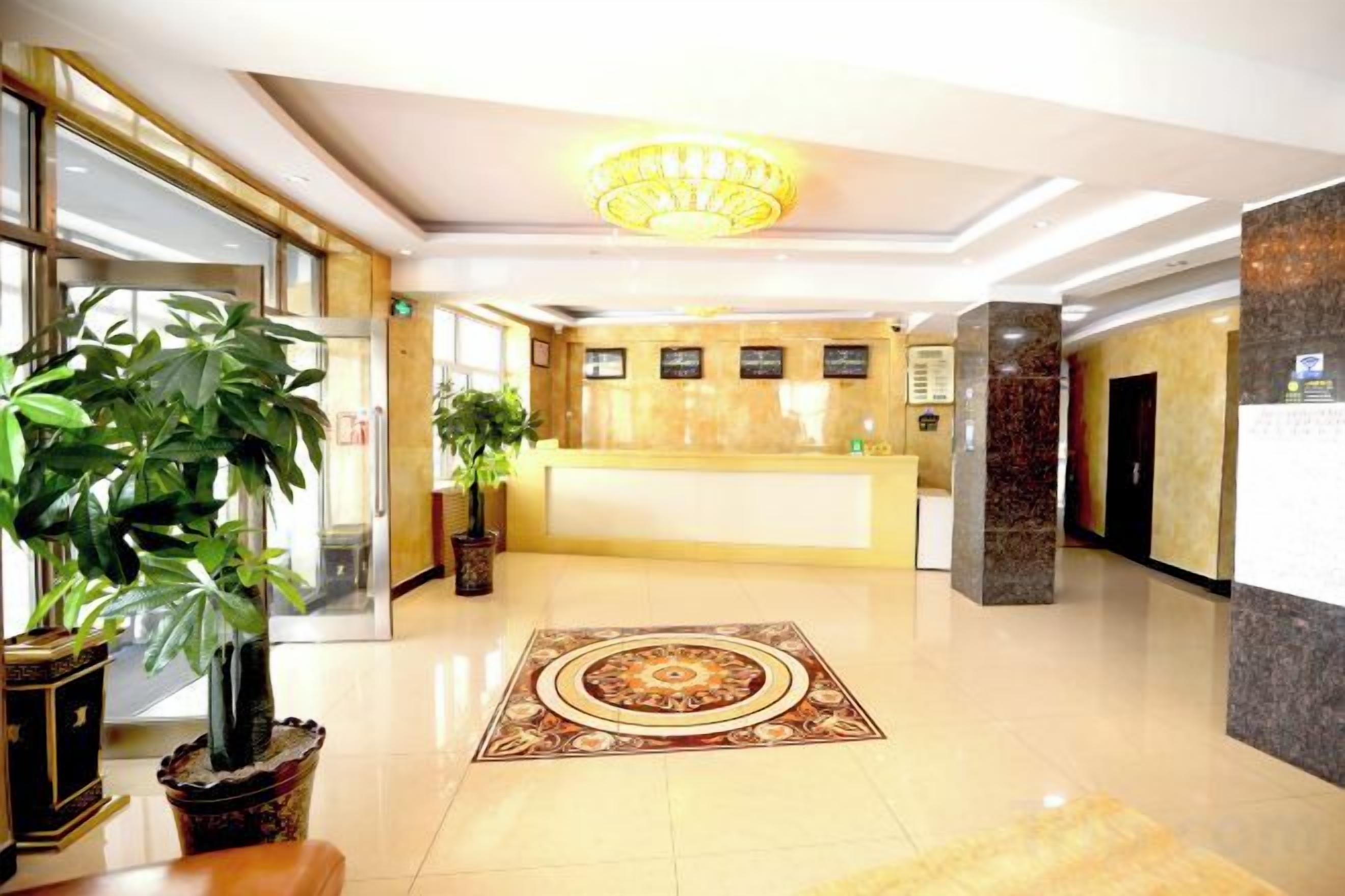 A hotel reception area with a reception desk, potted plants, and a decorative carpet.