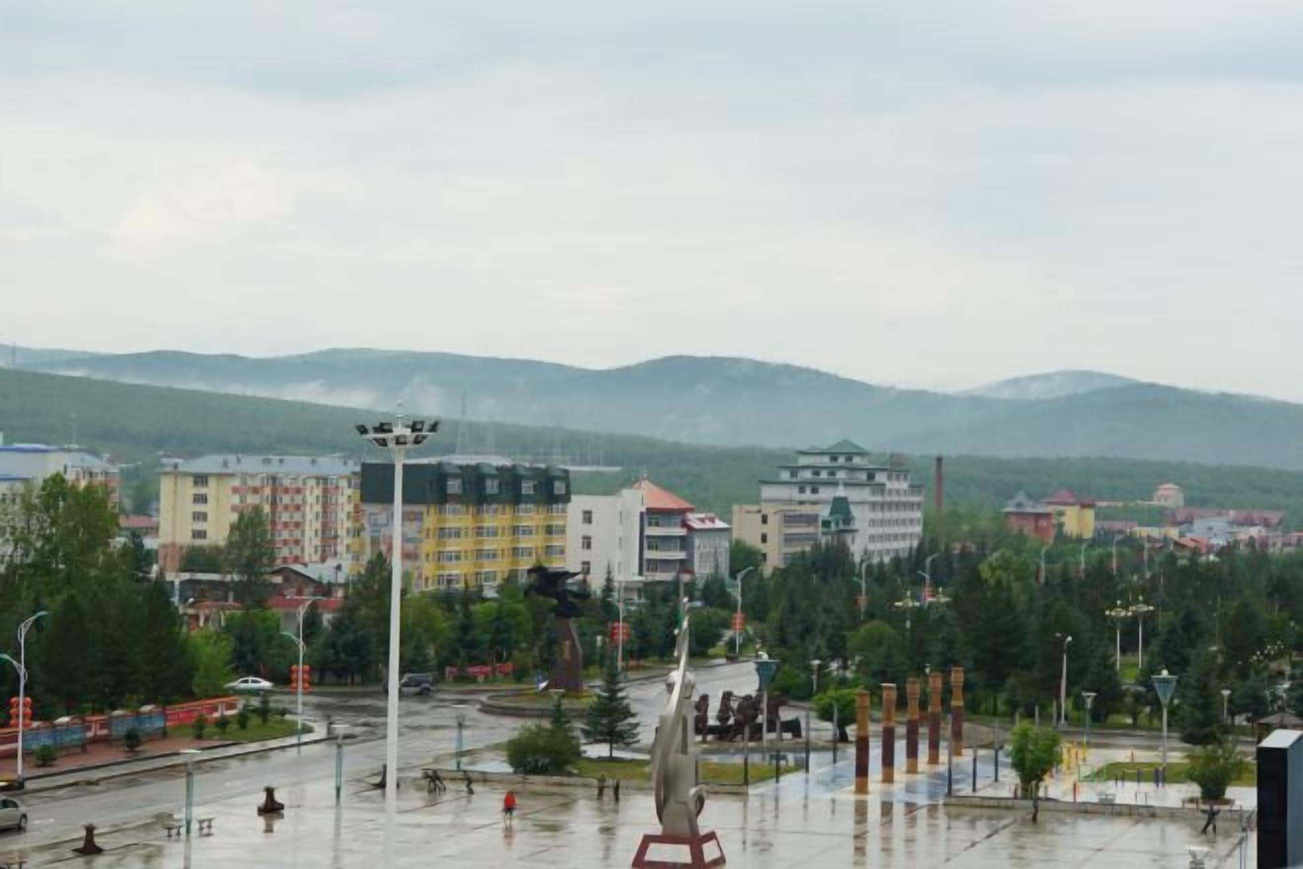Un paysage urbain avec des bâtiments, un espace vert aménagé en parc et une chaîne de montagnes à l’horizon.