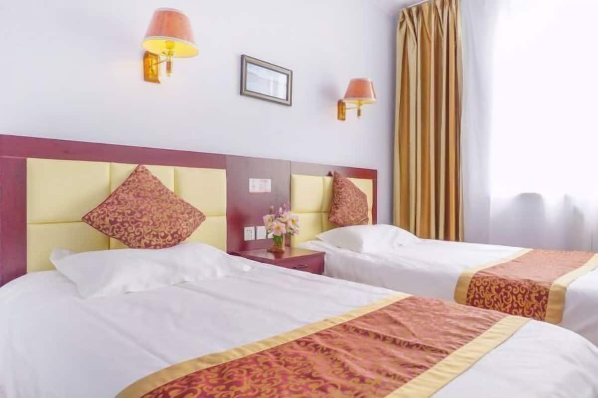 Een hotelkamer met twee bedden, elk met hoofdeinde, nachtkastje, lamp en een ingelijst beeld aan de muur.