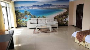Una habitación con un gran mural de una escena de playa, un sofá blanco, una mesita de centro y una cama con colcha estampada.