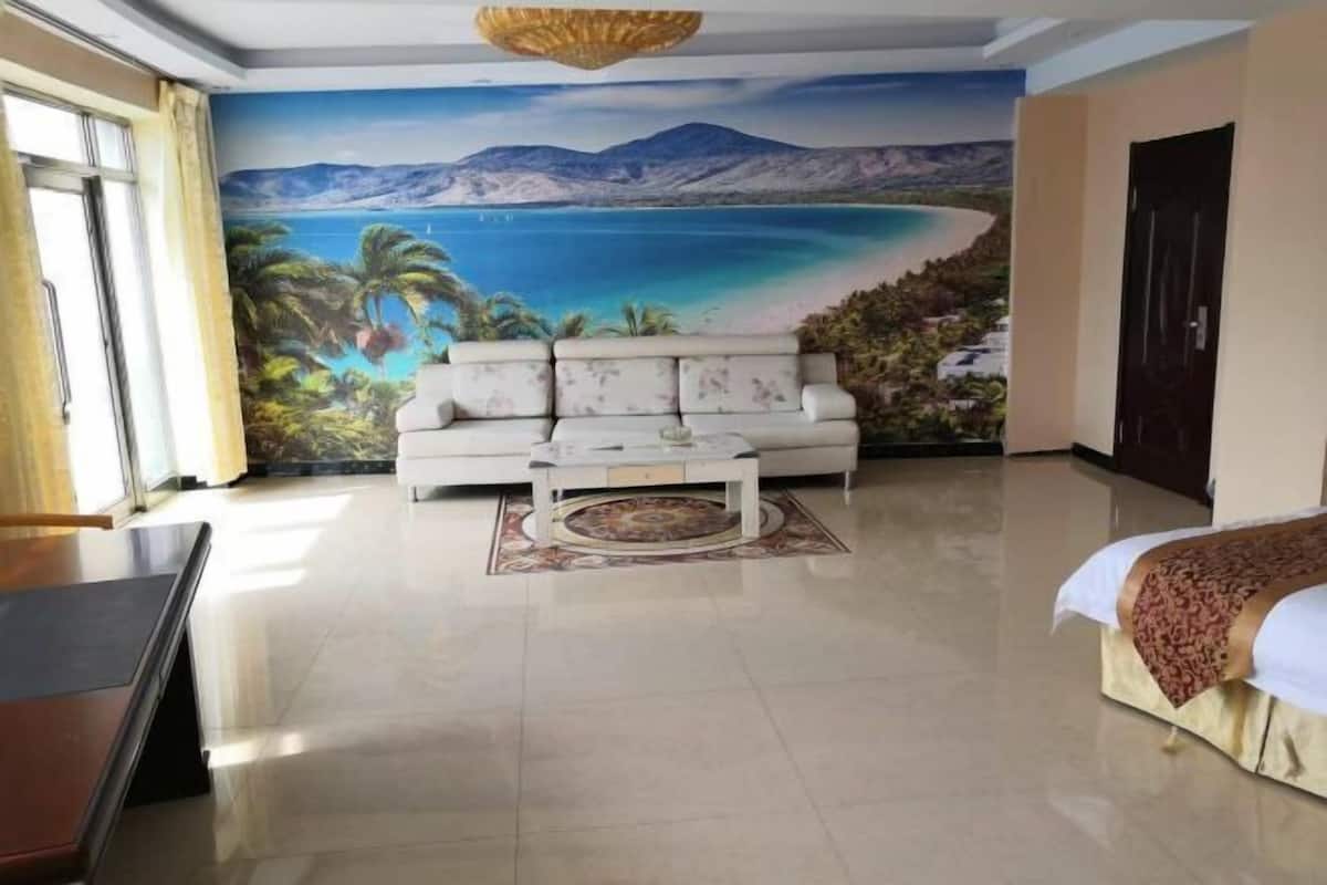 Een kamer met een groot muurschildering van een strand, een witte bank, een salontafel en een bed met een beddengoed met dessin.