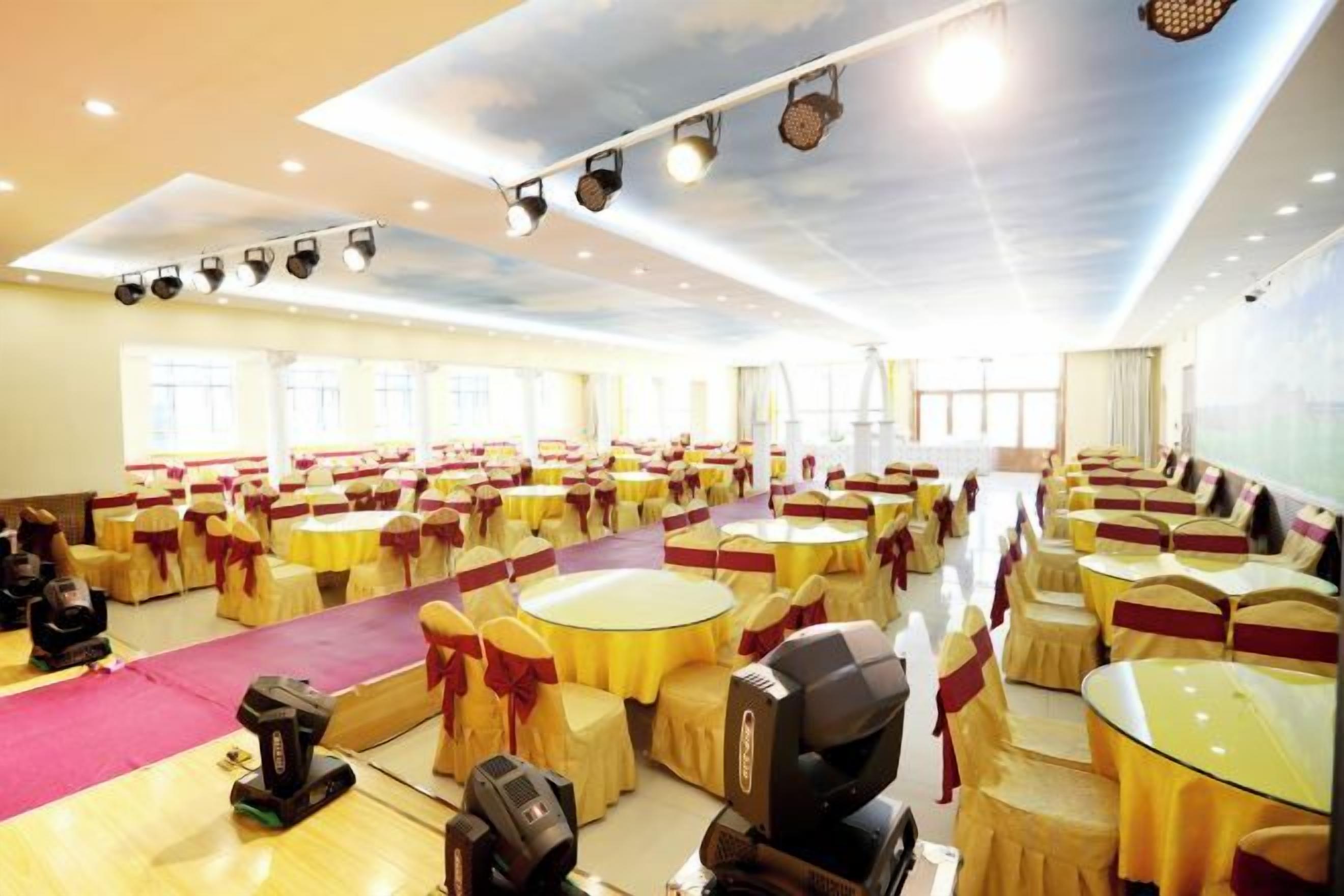 A large hall with round tables and chairs, arranged in rows, with a stage area at the front.