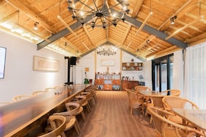 Un espace repas avec une longue table en bois et des chaises en osier, un lustre et un haut plafond en bois.