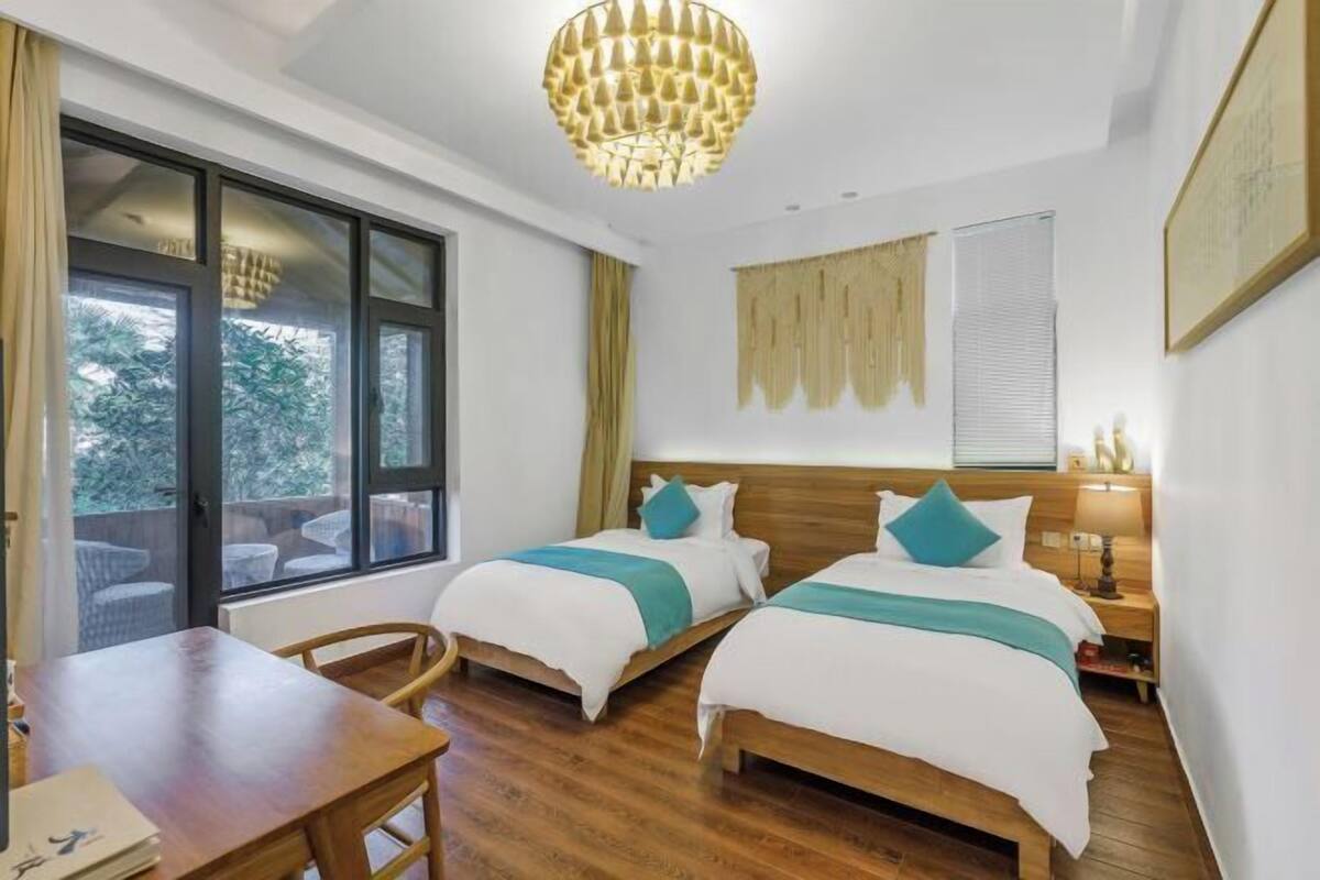 Une chambre d’hôtel avec deux lits, une table en bois, un lustre et de grandes fenêtres.