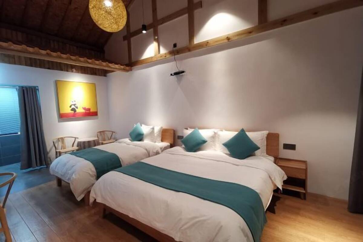 Une chambre avec deux lits, des poutres apparentes, un luminaire suspendu et un tableau au mur.