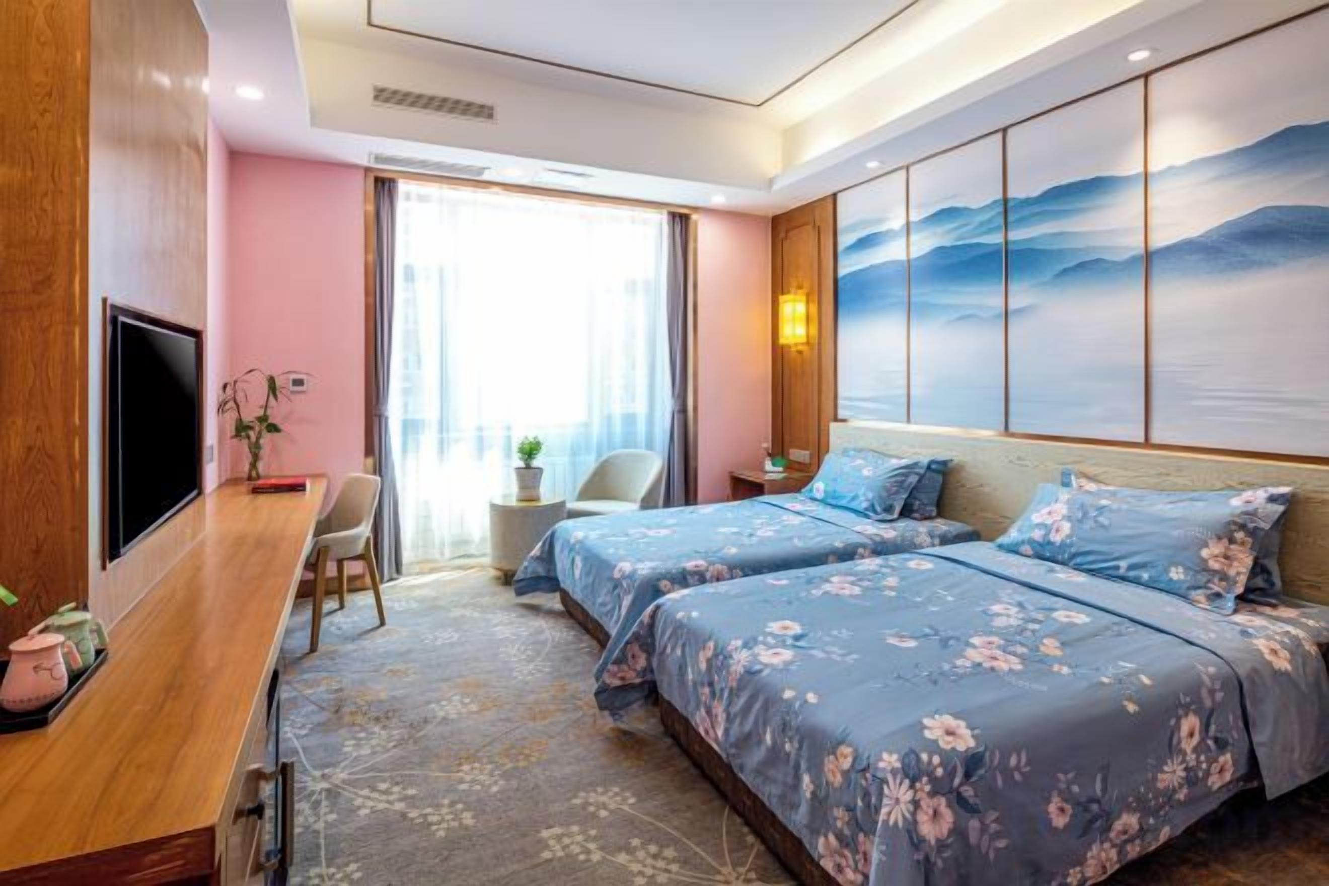 A hotel room with a bed, a desk, a chair, a television, and a painting on the wall.
