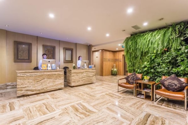Zona de recepción de un hotel con suelo de mármol, dos mostradores y un jardín vertical verde, además de asientos de cuero.
