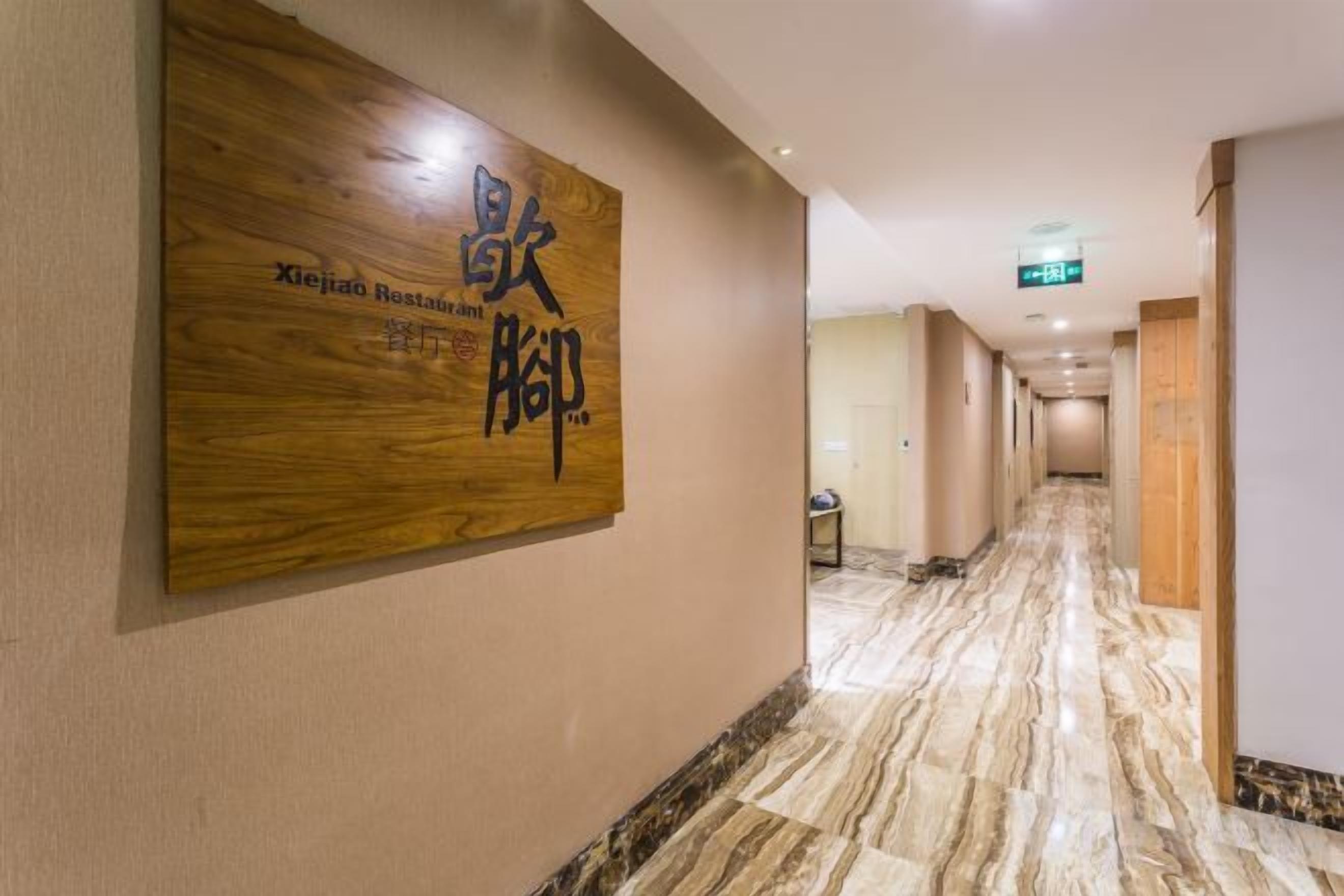 A hotel corridor with a wooden signboard, marble flooring, and a long hallway leading to a door.