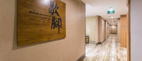 A hotel corridor with a wooden signboard, marble flooring, and a long hallway leading to a door.