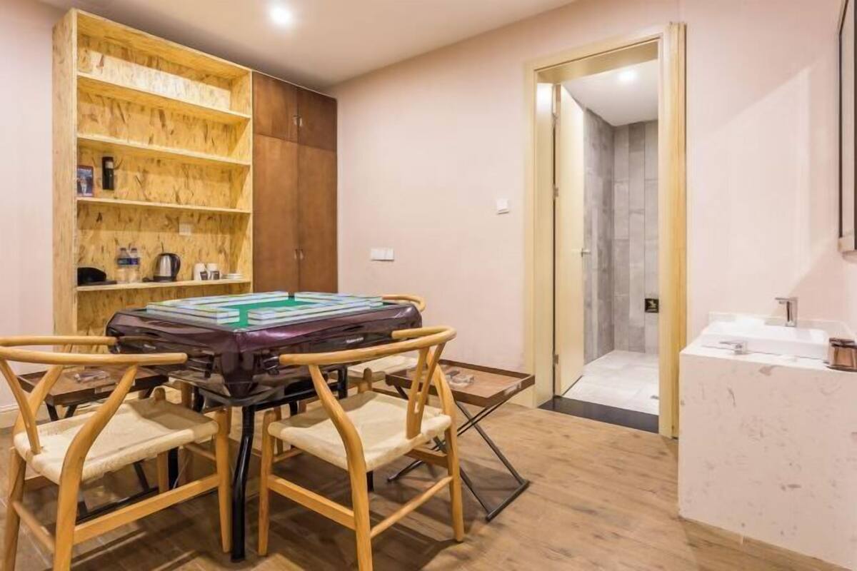 A room with a pool table, wooden chairs, a wooden shelving unit, and a bathroom visible through an open door.