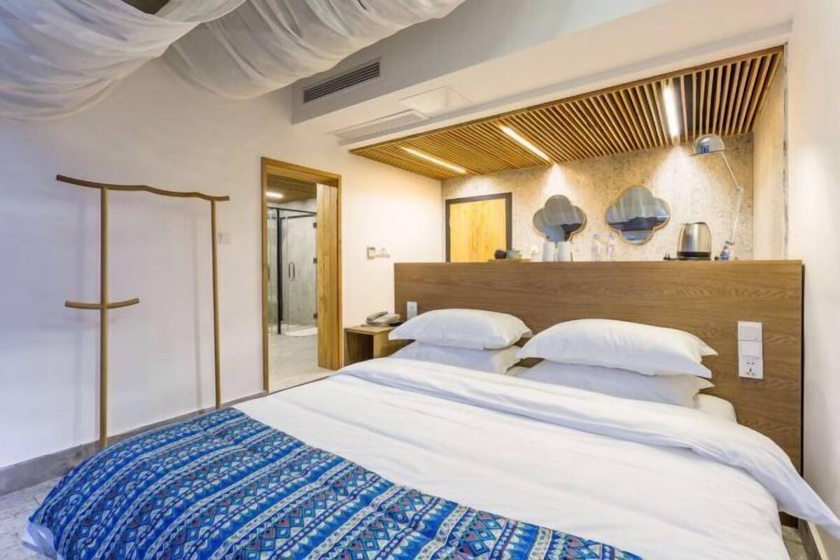 A hotel room with a bed, a wooden headboard, a mirror, and a bedside table.