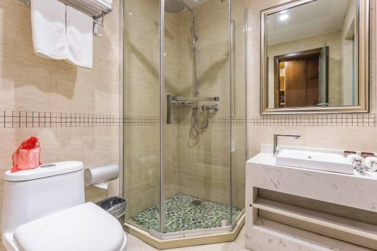 A bathroom with a glass-enclosed shower, a toilet, a sink with a marble countertop, and a mirror.
