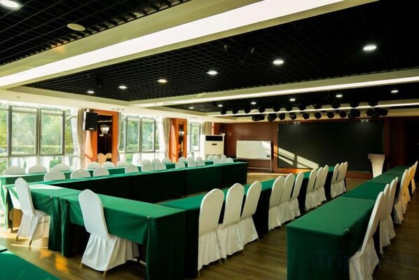 A conference room with long tables, chairs, a whiteboard, and a projector screen.
