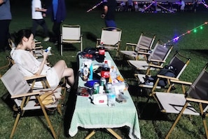An outdoor event with a table set up on grass, surrounded by chairs, and various items on the table. - Guli Hotel (Nanjing)