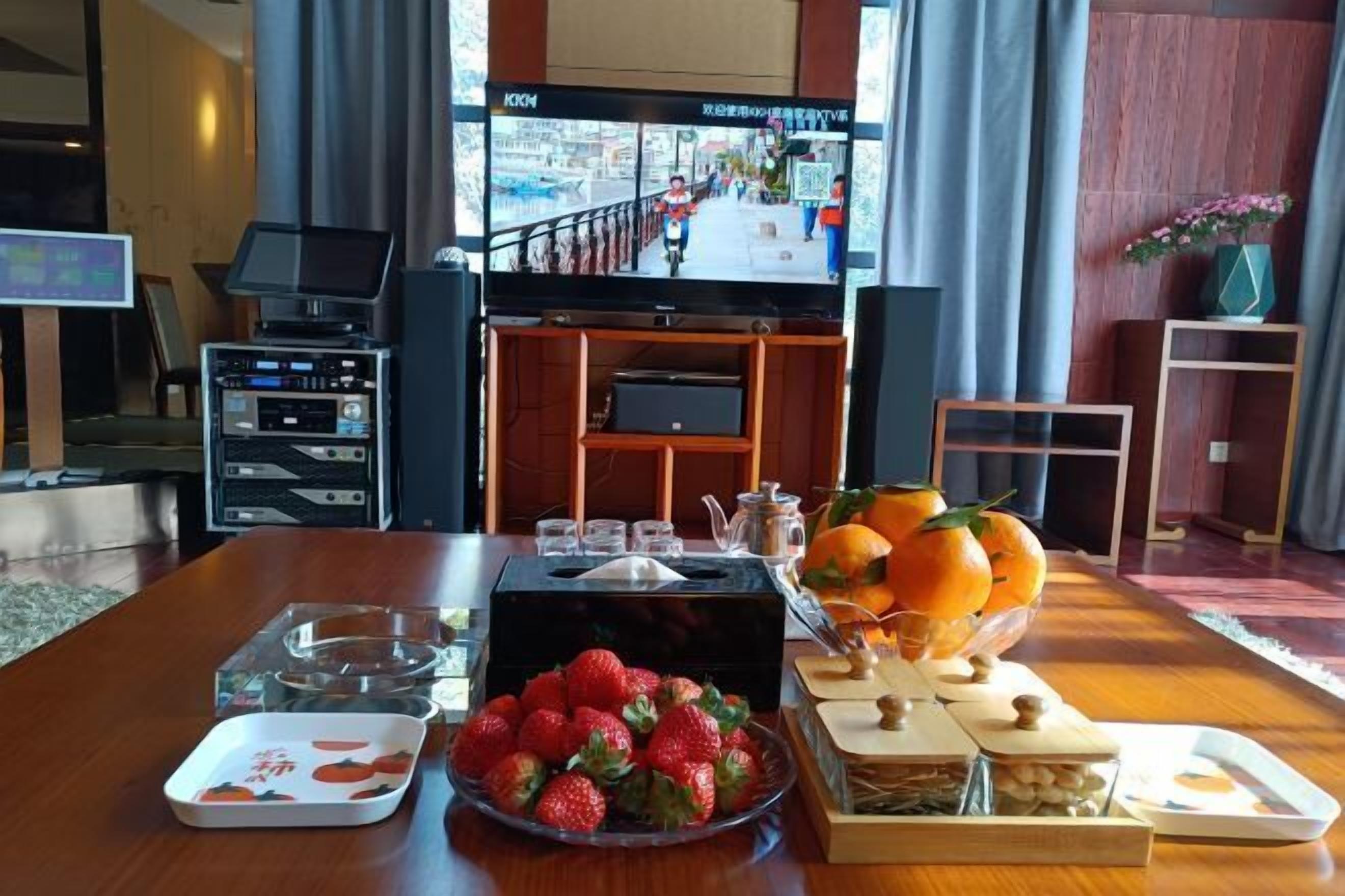 A hotel room with a wooden dining table set with fruit, a television, and a laptop.