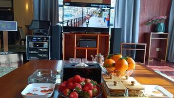 A hotel room with a wooden dining table set with fruit, a television, and a laptop.