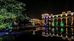 A hotel with a reflection pool, illuminated by lights, and a building with a traditional architectural style. - Guli Hotel (Nanjing)