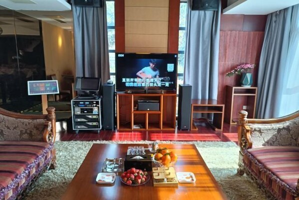 A living room with a television, wooden furniture, a coffee table with snacks, and a small side table. - Guli Hotel (Nanjing)