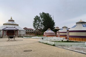 A courtyard with yurts, a white picket fence, and a large tree. - Guli Hotel (Nanjing)