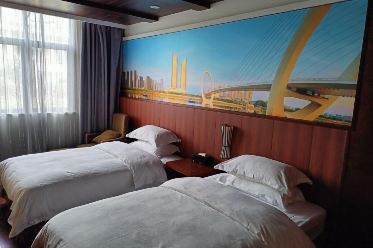 A hotel room with two beds, a large window with curtains, and a mural of a bridge.