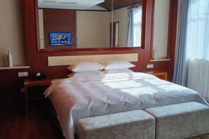 A hotel room with a bed, a nightstand, a mirror, and a television on the wall. - Guli Hotel (Nanjing)
