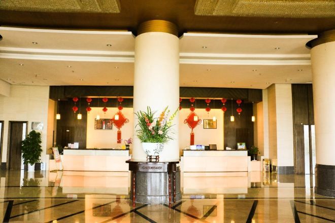 A hotel lobby with a reception desk, large columns, and a decorative plant.