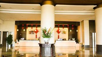 A hotel lobby with a reception desk, large columns, and a decorative plant.