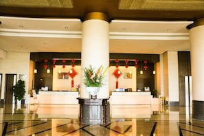 A hotel lobby with a reception desk, large columns, and a decorative plant. - Golden Eagle Hotel (Zhoushan)