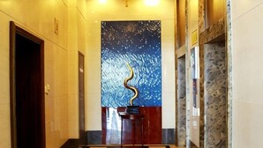 A hallway with a checkered floor, a blue wall with a decorative element, and a door on the left. - Golden Eagle Hotel (Zhoushan)