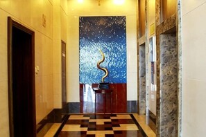 A hallway with a checkered floor, a blue wall with a decorative element, and a door on the left. - Golden Eagle Hotel (Zhoushan)