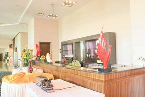 A hotel reception area with a reception desk, a seating area, and a large window. - Golden Eagle Hotel (Zhoushan)