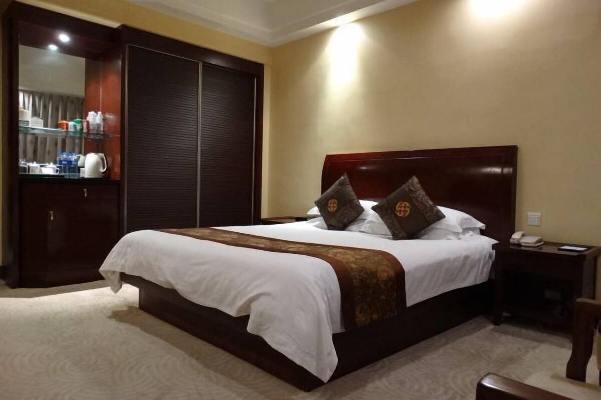 Ein Hotelzimmer mit einem großen Bett, einem Kleiderschrank, einem Nachttisch mit Telefon und einem Spiegel.