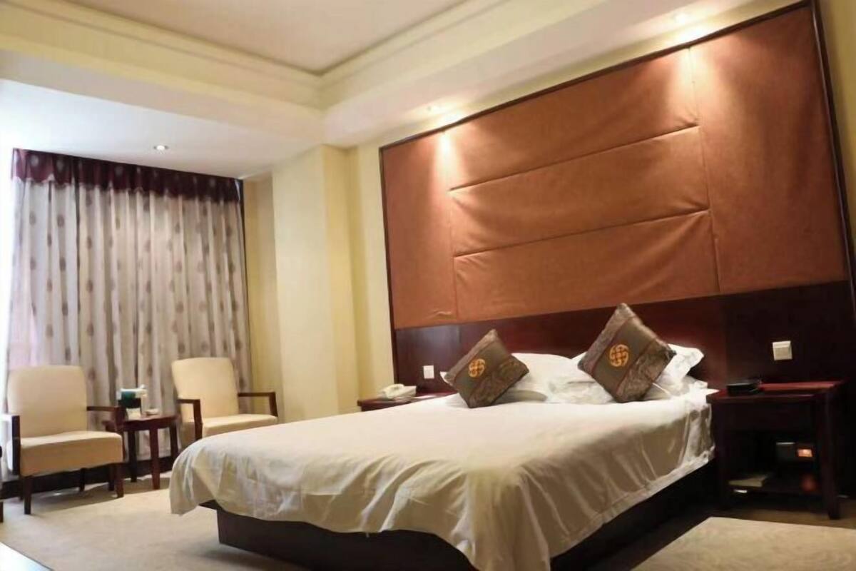 Ein Hotelzimmer mit einem großen Bett, zwei Sesseln, einem Nachttisch und einem Vorhang.