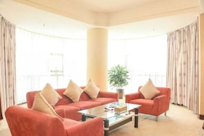 A living room with a red sofa set, a glass coffee table, and a potted plant. - Golden Eagle Hotel (Zhoushan)