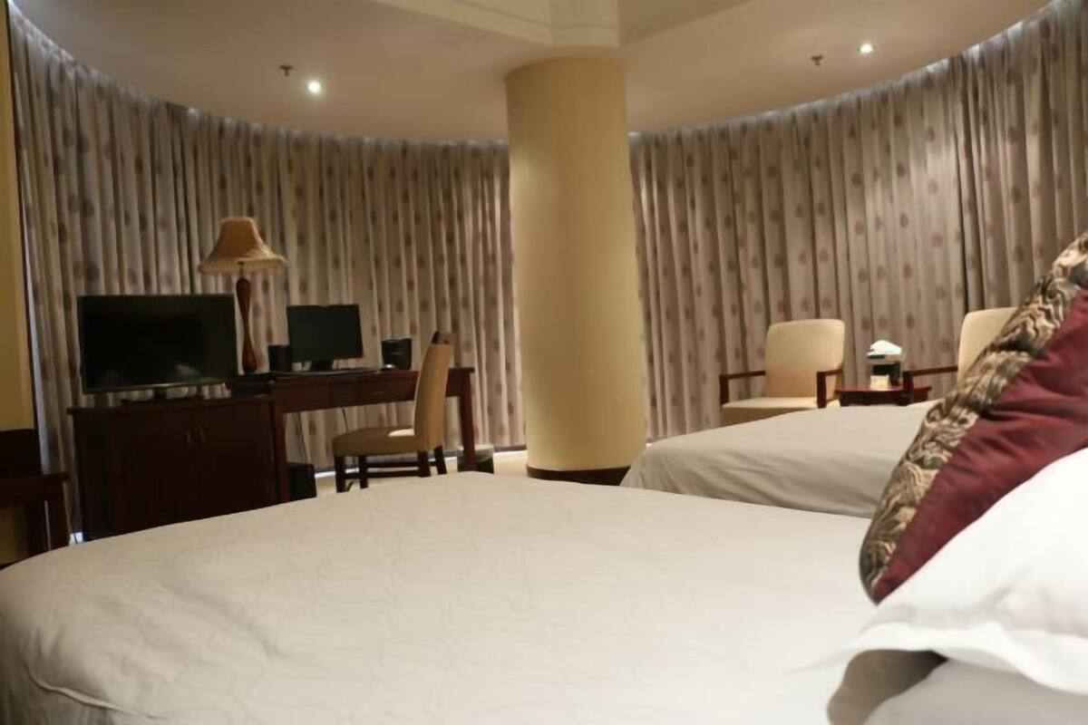 Ein Hotelzimmer mit einem großen Bett, einem Schreibtisch mit Computer, einem Sessel und einem Fernseher.