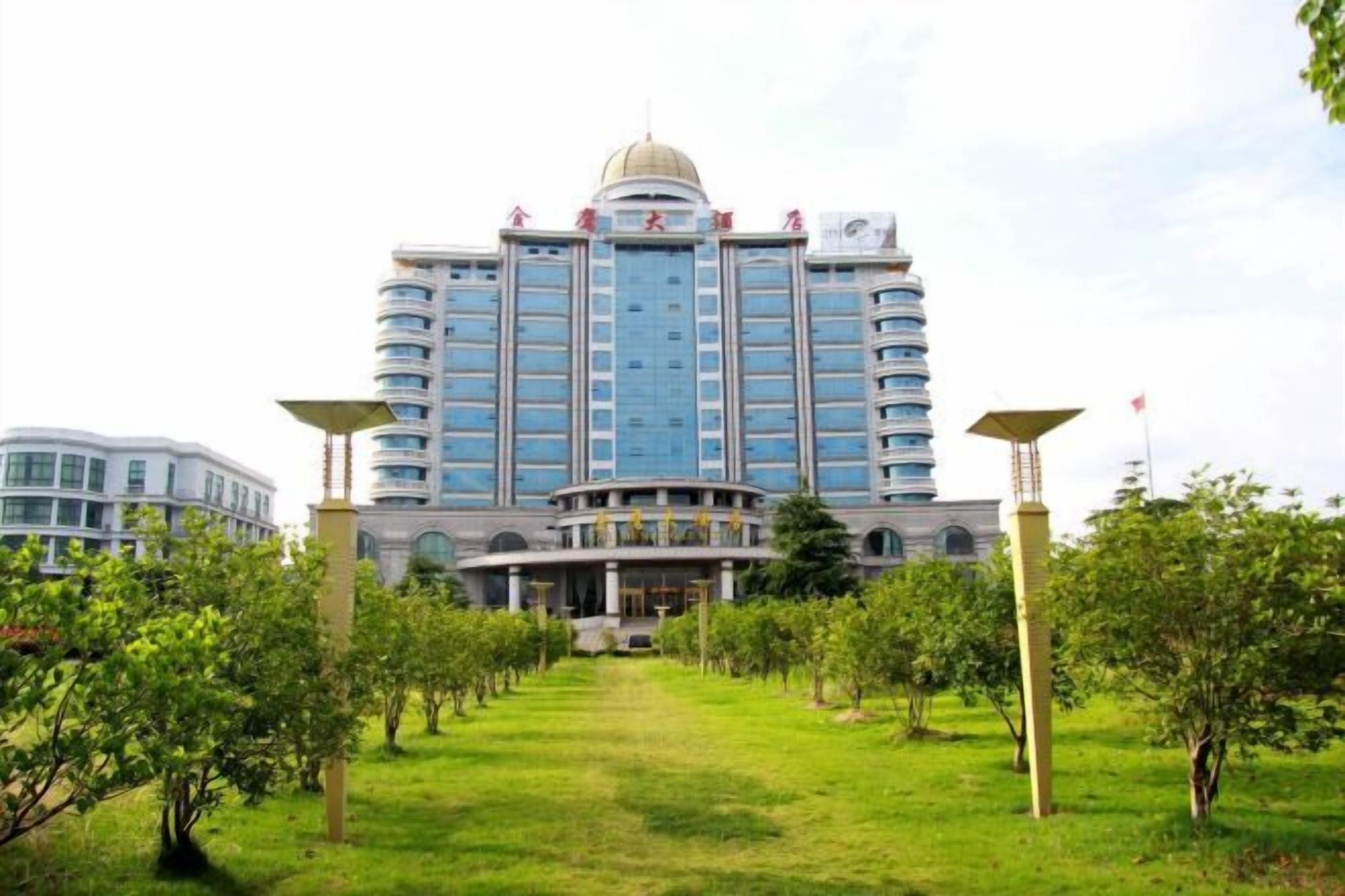 Un hotel grande con una cúpula central y varios pisos, rodeado de césped cuidado y árboles.