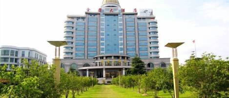 Un hotel grande con una cúpula central y varios pisos, rodeado de césped cuidado y árboles.