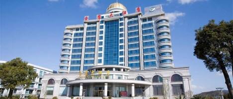 Un hotel de varios pisos con una cúpula central, una entrada amplia y un jardín frontal ajardinado.