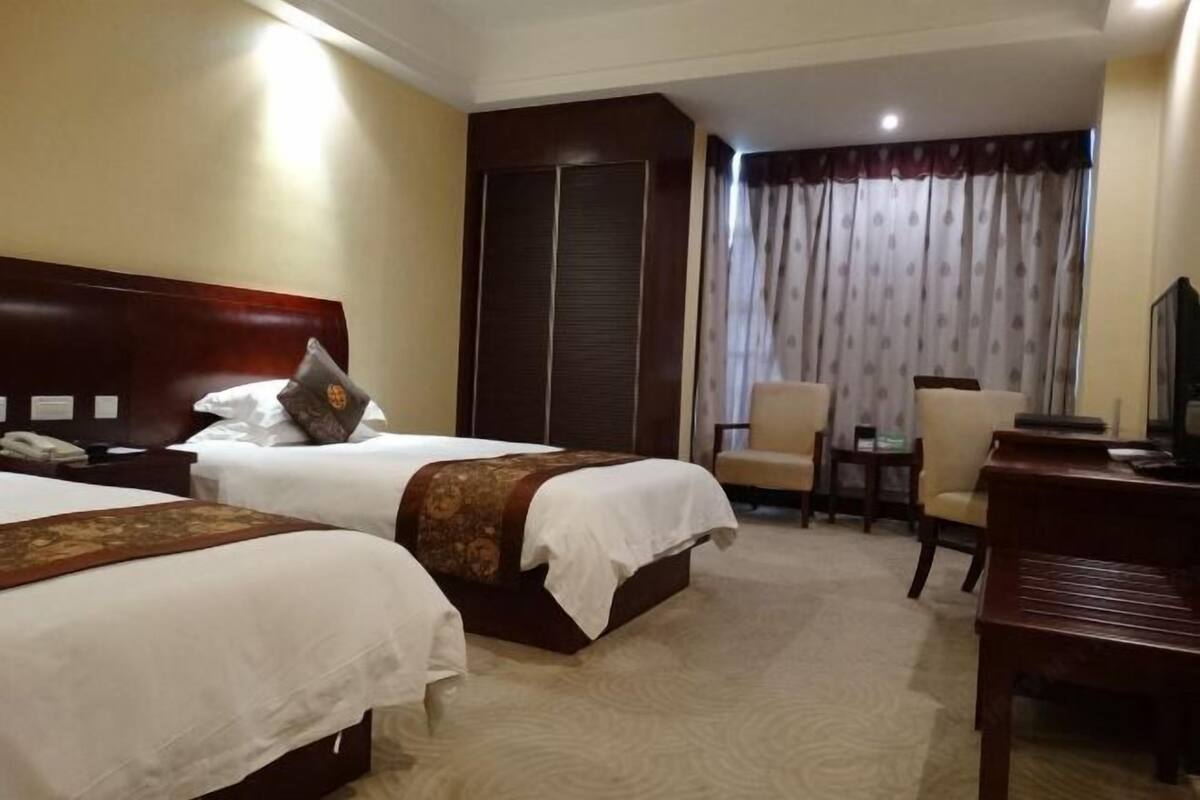 Ein Hotelzimmer mit zwei Betten, einem Schreibtisch, einem Sessel und einem Fernseher.