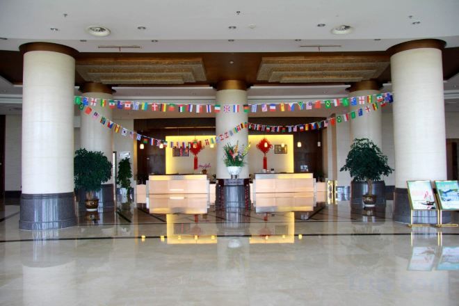 A hotel lobby with a reception desk, large pillars, and potted plants.