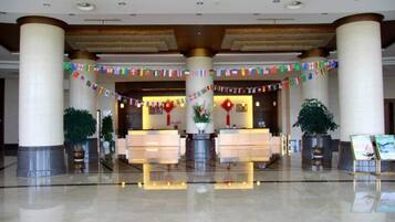 A hotel lobby with a reception desk, large pillars, and potted plants.