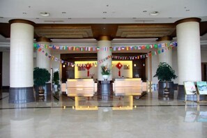 A hotel lobby with a reception desk, large pillars, and potted plants. - Golden Eagle Hotel (Zhoushan)