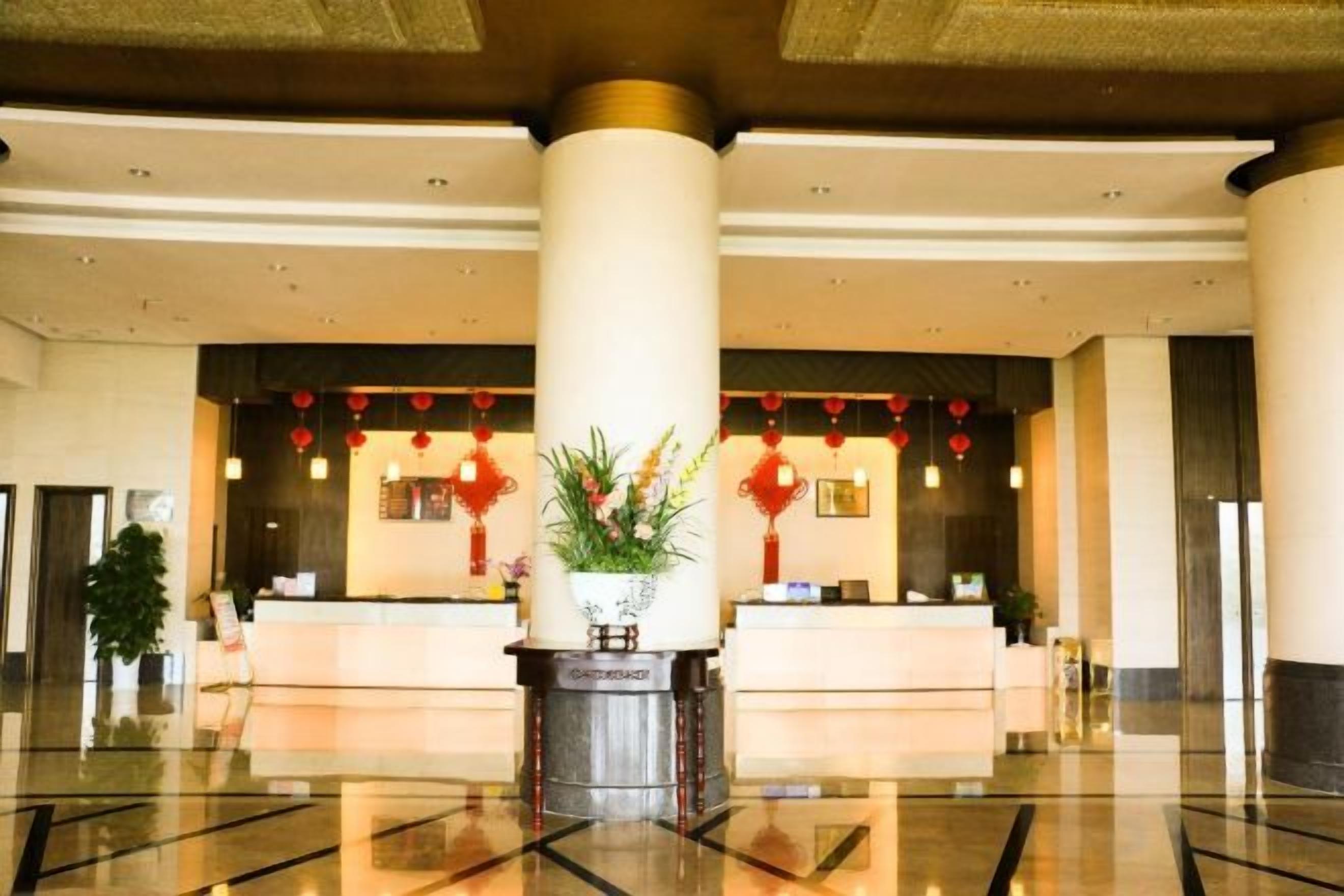 Un vestíbulo de hotel con mostrador de recepción, columnas grandes y suelo pulido.