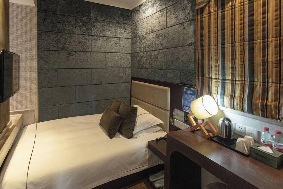 Ein Hotelzimmer mit einem Bett, einem Nachttisch mit Lampe, einem Fernseher und einem Fenster mit Vorhängen.