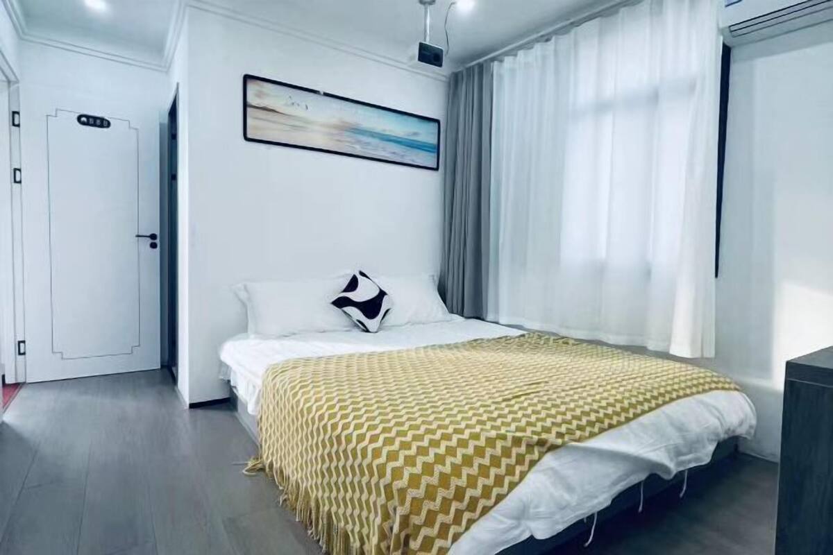 A hotel room with a bed, a door, a painting, and a window with curtains.
