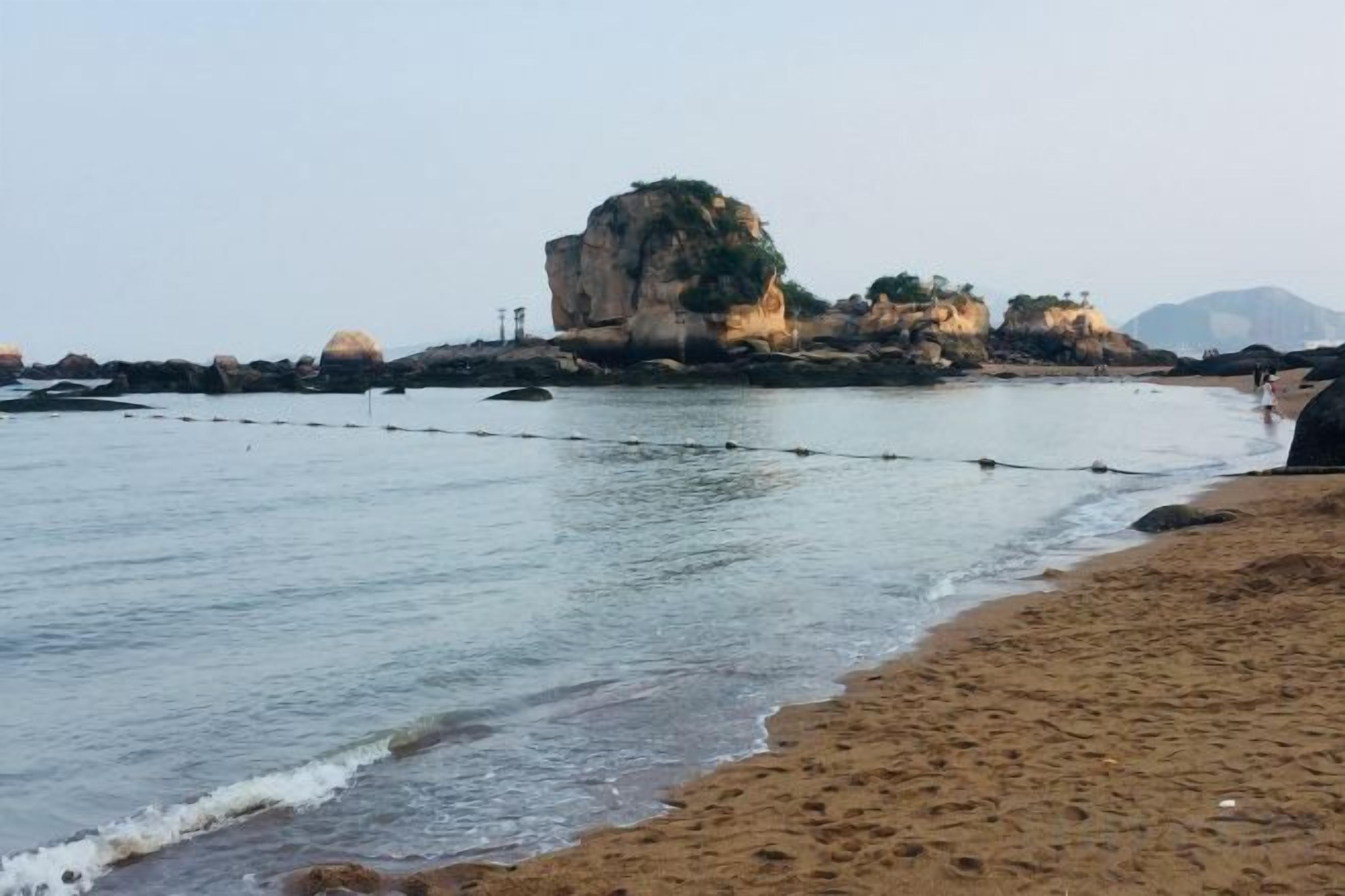 A beach with a rocky outcrop and calm water.