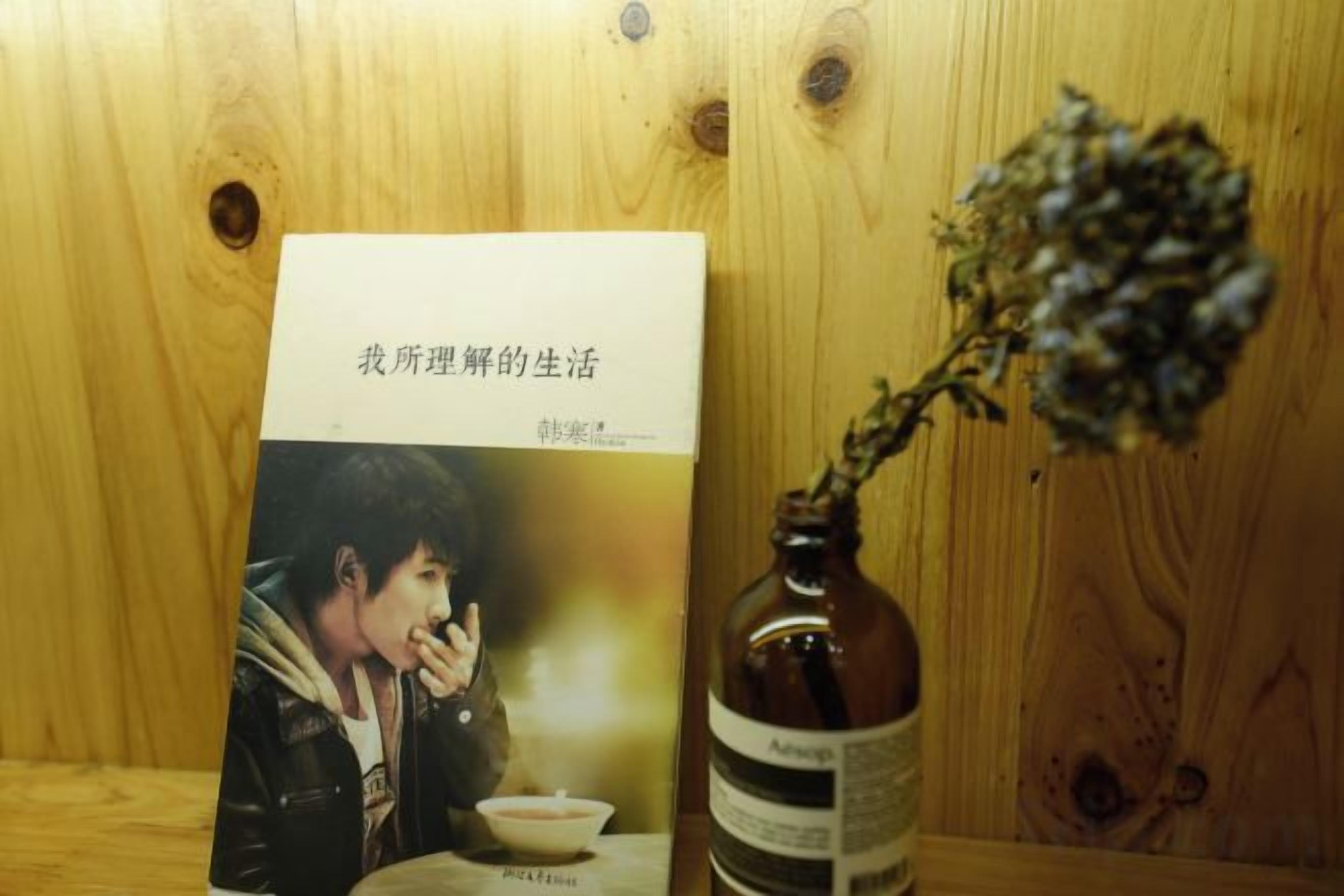 Un libro con el título 'I understand my life' junto a una botella de agua y una flor seca sobre una superficie de madera.